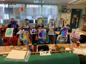 Kids holding up art projects in a classroom