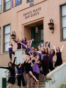 A group of women dancers posing on outside steps with their arms stretched up into the air.